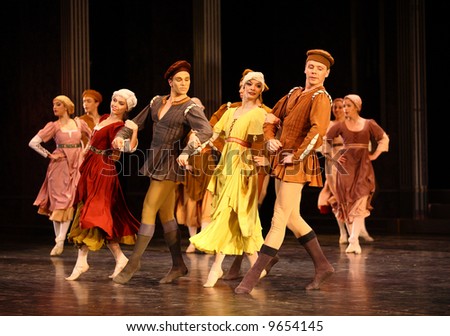group of classic ballet dancers dancing holding hands lit by stage lights