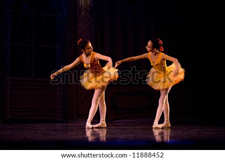 two classic ballet girl dancers in yellow dresses bow on stage lit by stage light