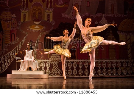 two classic ballet female dancers on stage standing on one leg lit by stage light