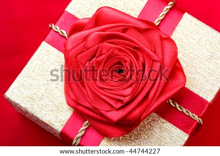 Gold box on a red background with a red ribbon rose