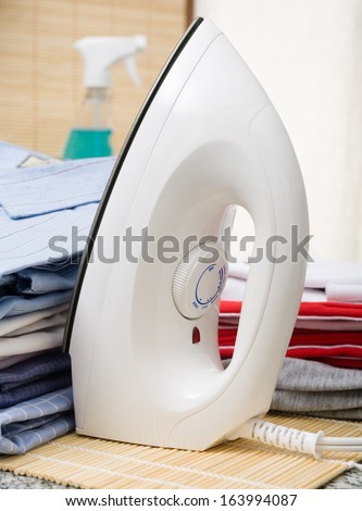 An iron next to a pile of ironed clothes.