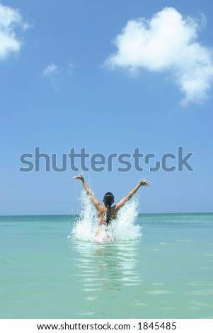 Girl splashing out of the ocean with her arms reaching to the blue sky