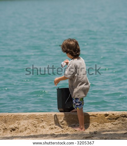 young boy with a fish in his hand putting it in a bucket