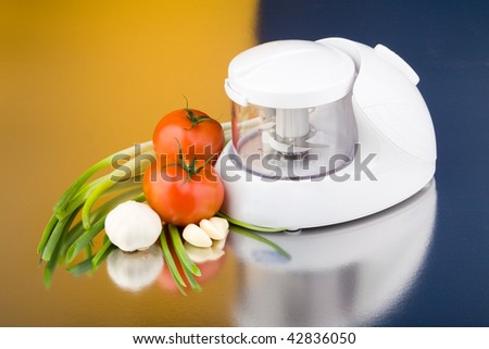 Food processor with  tomatoes, onions and garlic on colorful  background