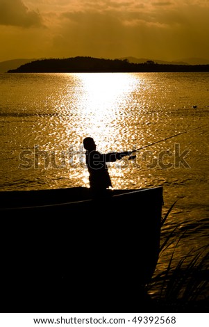 Silhouette of a man in a boat fishing with a beautiful lake background at sunset