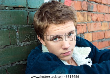 Portrait of the young and pretty boy sitting near the grunge wall