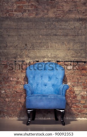 An antique blue velvet chair near the grungy brick wall