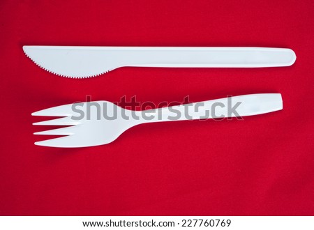 White plastic fork and knife , fork and knife on red background.