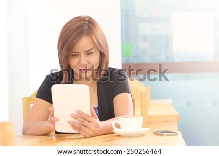 Asian woman use Tablet or Smartphone has coffee cup her left hand in the morning at restaurant
