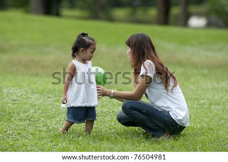 Mother teaching daughter to soccer/ball in the park happily.