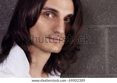 Closeup portrait of a young handsome man in white shirt against brick wall background