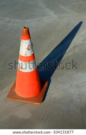An orange traffic cone casts a long early morning shadow on newly poured concrete floor