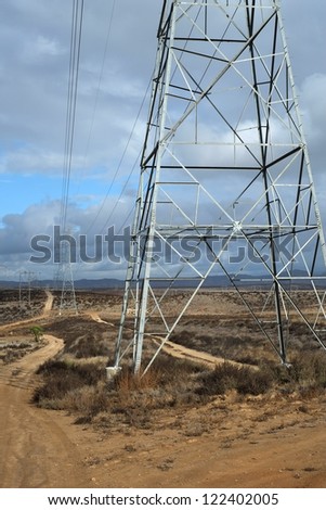 High voltage power lines and access road stretch across the California high desert toward the stormy Sierra Nevada Mountains