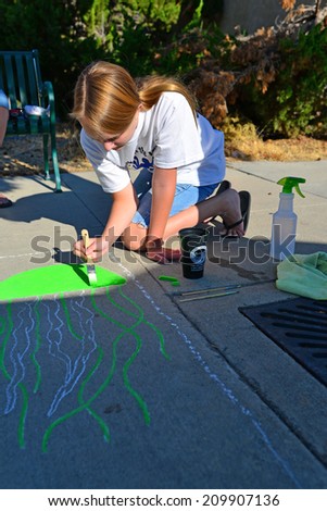 TEHACHAPI, CA - AUGUST 9, 2014: Autumn Shackelford has already laid out here drawing on the sidewalk and begins to add color to her creation for the annual Chalk on the Walk art contest.