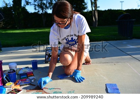 TEHACHAPI, CA - AUGUST 9, 2014: Lori Martin has already laid out here drawing on the sidewalk and begins to add color to her creation for the annual Chalk on the Walk art contest.