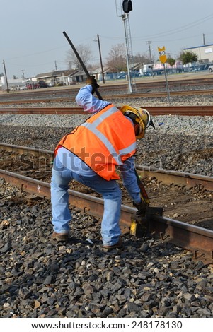 BAKERSFIELD, CA - JANUARY 29, 2015: Two Union Pacific Railroad employees position a tool on a rail to assist in replacing old wood tie with a new one.