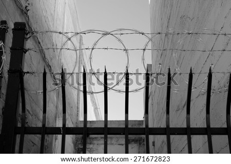 An inner city fence with sharpened vertical bars, barbed wire and concertina wire conveys the message. \