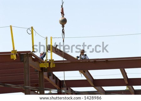 Iron workers receive a beam lifted by crane on construction job site
