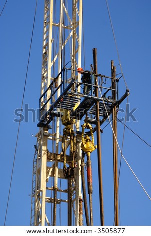 Roustabout works on high platform of oil drilling rig, Kern County, California