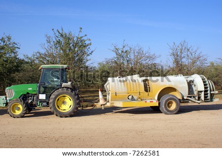 Tractor and insecticide spraying trailer in almond groves, San Joaquin Valley, California