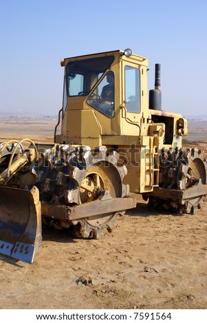Tractor with blade and sheepshead rollers prepares site for new construction