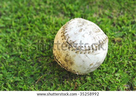 A well-used and abused softball lying on the outfield grass