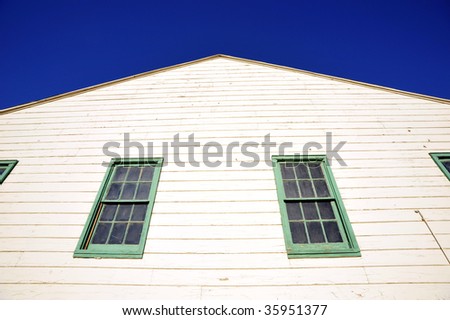 Simple old white painted wooden building with green trimmed windows against deep blue sky