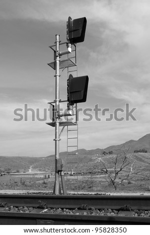Black and white image of railroad standard with hooded signal lights in western landscape