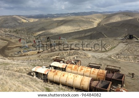 Old oil field heaters are in the foreground while downhill a group of oil wells are located in the foothills of the Sierra Nevada, California
