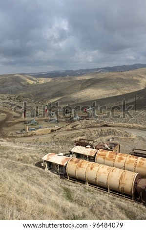 Old oil field heaters are in the foreground while downhill a group of oil wells are located in the foothills of the Sierra Nevada, California