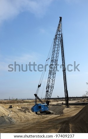 Long mast of crane supports hydraulic ram pile driver on construction project