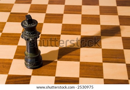 King chess piece (with shadow) on a fine, wooden chess board with a dark and a light stain
