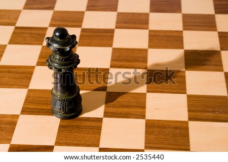 Queen chess piece (with shadow) on a fine, wooden chess board with a dark and a light stain