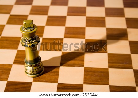The king chess piece (with shadow) on a fine, wooden chess board with a dark and a light stain
