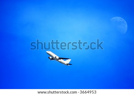 Plane flying overhead with the moon and a bluish sky in the background.