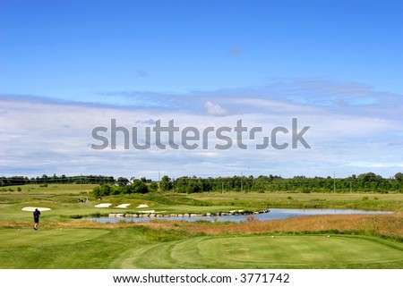 Wide view of a golf course with thick rough, trees, sand and water hazards.