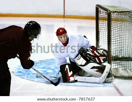 Goalie in generic white jersey with generic red goalie mask makes a tremendous attempt to prevent the puck (under the blocker) from entering the goal