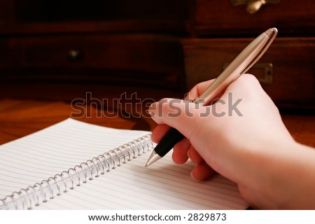 A hand writing on a pad of paper on a wooden desk.