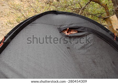 Young woman looks out of tent during a rain. Self portrait.