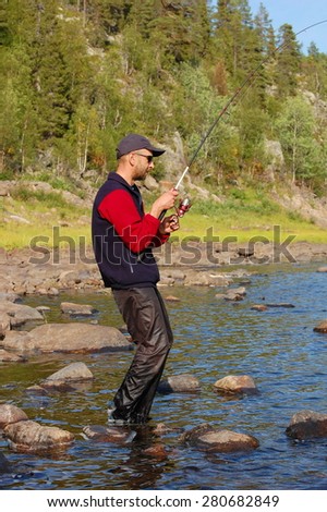 Fisherman catches a salmon in the north river. Varzuga river, Kola Peninsula, Russia.