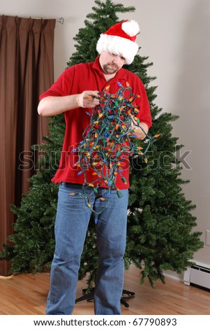 A man attempts to untangle a string of Christmas lights in front of an undecorated Christmas Tree.