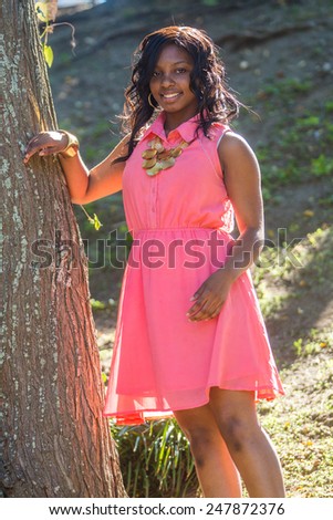 smiling happy beautiful african american teenage girl in pink dress in the park