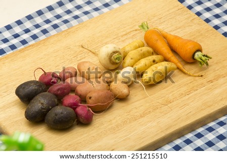 a variety of fresh local organic artisanal produce from small farms laid out on a cutting board purple potato, beets, potato, turnip, more potatos, then carrots ingredients for potato dish