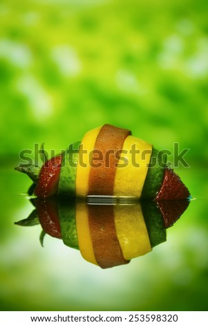 slices of strawberry cucumber, squash, and sweet potato assembled into one super fruit-vegetable mash-up on lushious green background with reflection underneath
