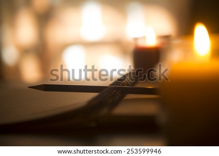 Artist\'s drawing notebook with pencil, lit by candles.