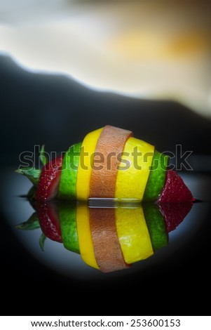 slices of fruits and vegetables formed into a frankenstein fruit on water with reflection