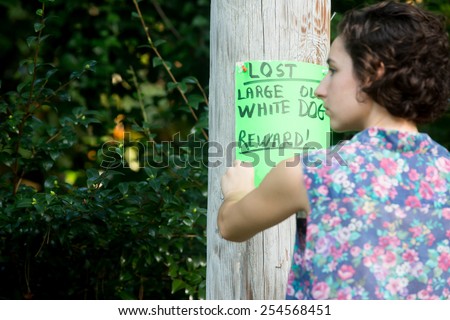 young woman posting lost dog sign on telephone pole