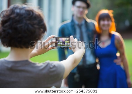 young couple being photographed in front of white house by female using smart phone
