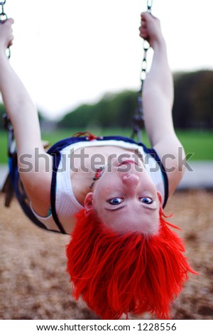 A young woman hanging upside down in a swing with her bright red hair dangling down.