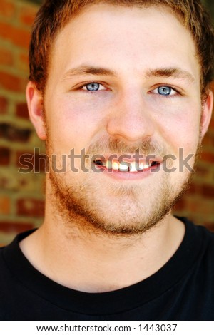 A young man with a scragly beard and blue eyes smiling.